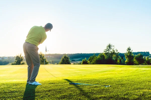 Golfista masculino experiente batendo a bola de golfe em direção ao copo — Fotografia de Stock