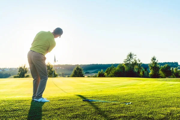 Golf masculino experimentado golpeando la pelota de golf hacia la copa — Foto de Stock