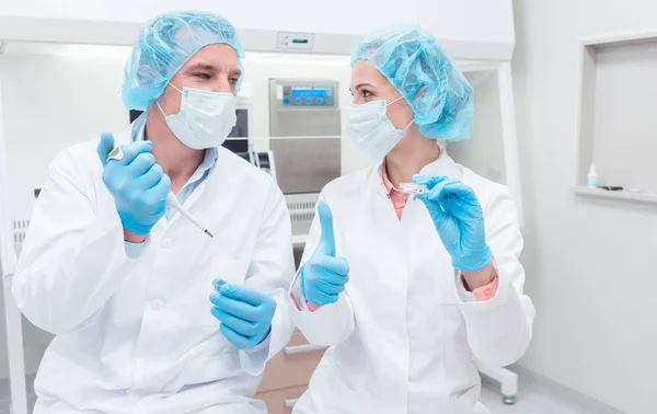 Cientistas em laboratório de biotecnologia com pipeta e prato de amostra — Fotografia de Stock