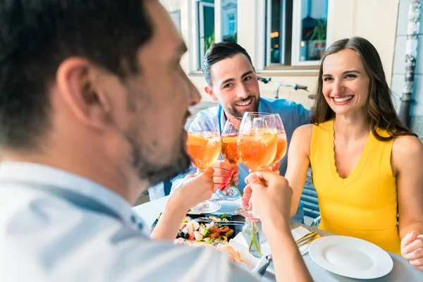 Zwei glückliche junge Paare stoßen beim gemeinsamen Sitzen in einem Restaurant an — Stockfoto