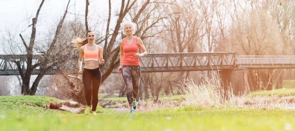 Seniorin und junge Frau laufen im Frühjahr als Sport auf einer Wiese — Stockfoto