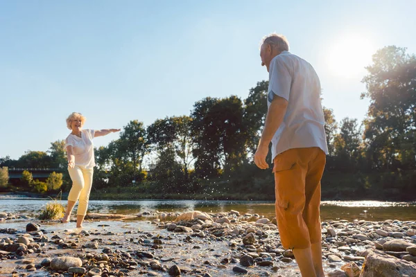 Αστεία ανώτερος ζευγάρι παίζει με το νερό στον ποταμό σε μια ηλιόλουστη μέρα — Φωτογραφία Αρχείου