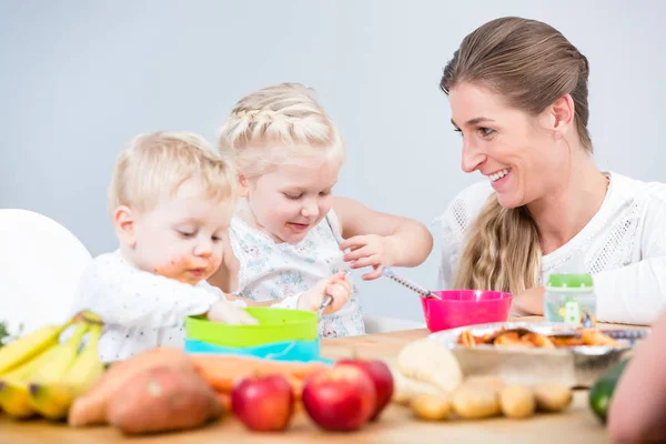 Portrait of a happy mother of two children sitting at table — Stock Photo, Image