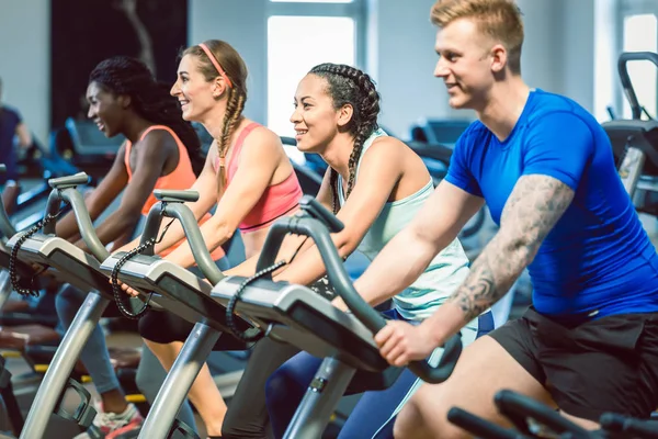 Vista laterale di una bella donna sorridente mentre pedala in palestra — Foto Stock