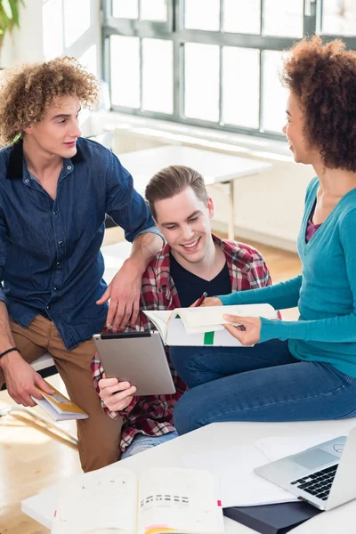 Trois jeunes étudiants utilisant à la fois un livre et une tablette PC pour vérifier les informations — Photo