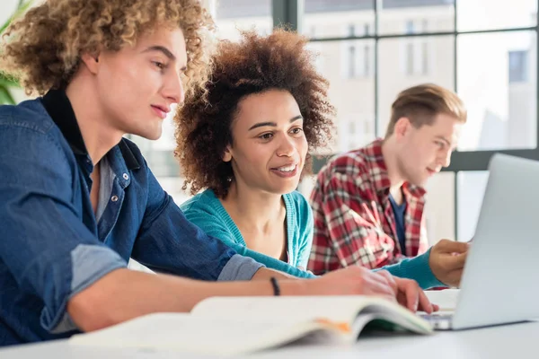 Fröhliche Frau, die eine Aufgabe schreibt, während sie zwischen zwei Klassenkameraden sitzt — Stockfoto