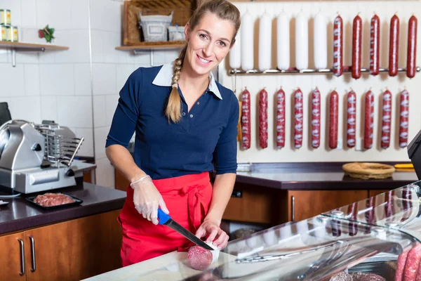 Carnicera cortando una salchicha en la tienda — Foto de Stock