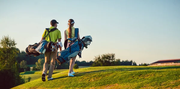 Pareja feliz vistiendo trajes de golf mientras lleva bolsas de pie —  Fotos de Stock