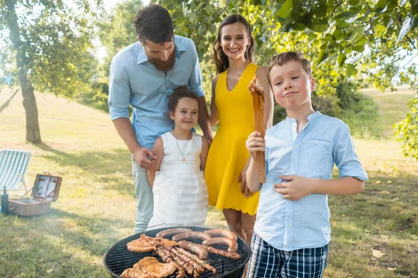 Ritratto di famiglia felice con due bambini in piedi all'aperto vicino a un barbecue — Foto Stock