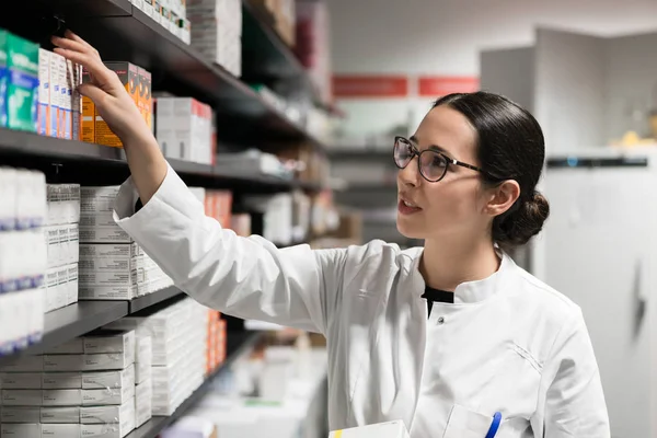 Dedicated pharmacist taking a medicine from the shelf during work — Stock Photo, Image