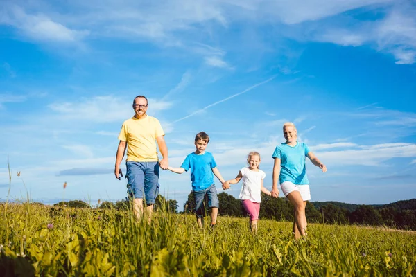 Familia cogida de la mano corriendo sobre el prado — Foto de Stock