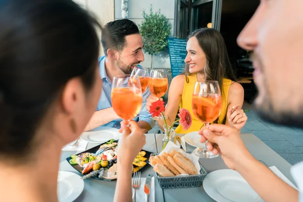 Dwie młode szczęśliwe pary, opiekania razem siedząc w restauracji — Zdjęcie stockowe