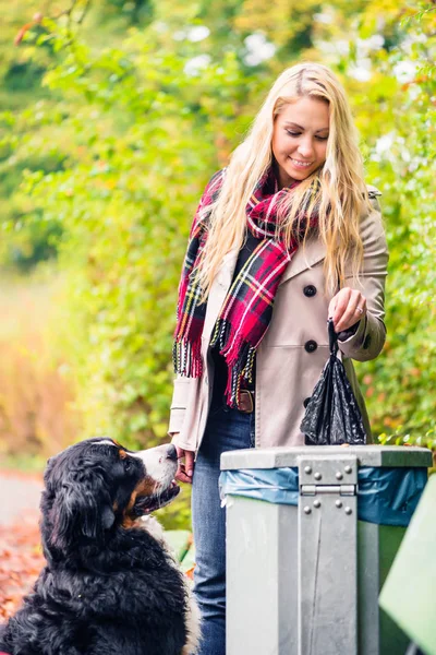 La mujer está recogiendo caca de perro poniéndola en la basura. — Foto de Stock