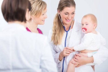 Kadın doktor onun kollarında bir kız şirin bebek tutan adanmış 