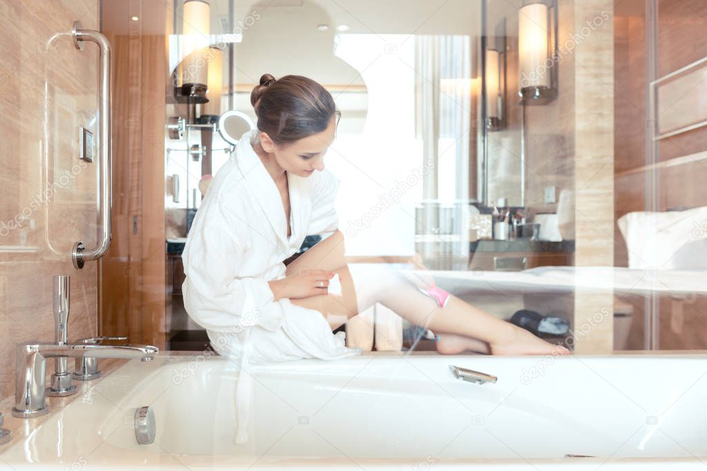 Woman removing hair by shaving her legs in bathroom of hotel
