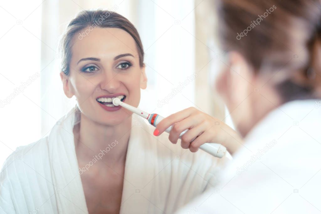 Woman brushing her teeth in luxurious hotel looking at herself