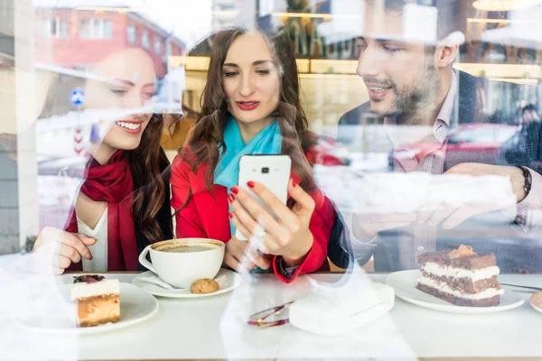 Mulher jovem na moda mostrando aos seus melhores amigos fotos no celular — Fotografia de Stock