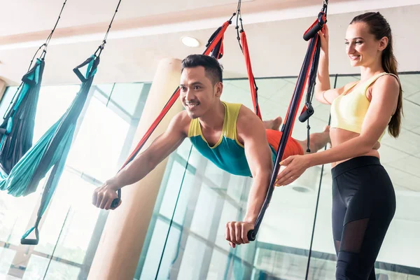 Joven alegre practicando yoga volador ayudado por su hermosa pareja —  Fotos de Stock