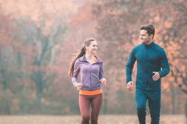 Harika sonbahar manzarası olan bir çift daha iyi spor yapmak için koşuyor.