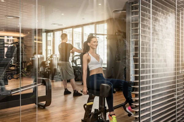 Attractive woman sitting at the abductor machine while exercising for buttocks — Stock Photo, Image