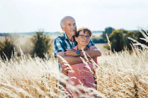 Старший мужчина обнимается с женой в траве — стоковое фото