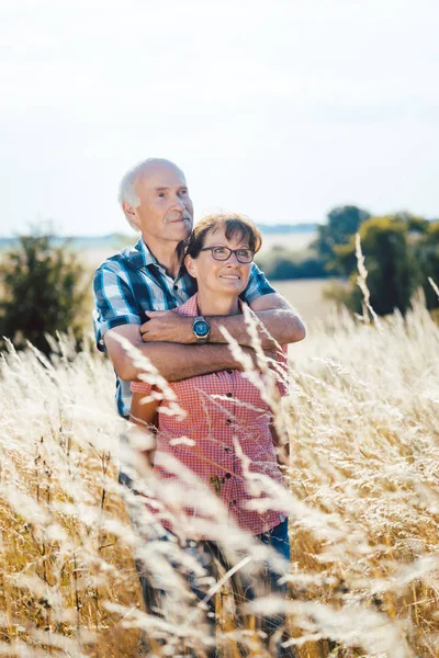 Старший мужчина обнимается с женой в траве — стоковое фото