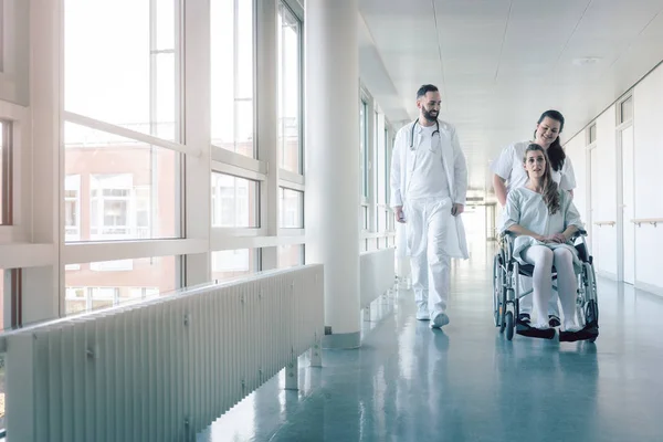 Doctor, nurse, and patient in wheelchair on hospital corridor — Stock Photo, Image