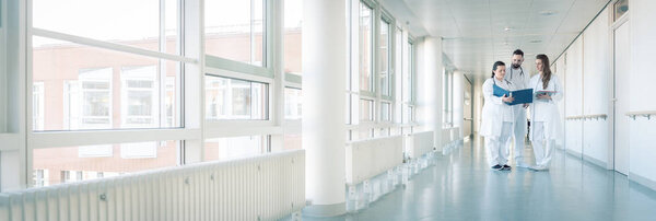 Three doctors on hospital corridor having short meeting 