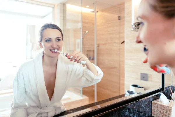 Женщина чистит зубы в роскошном отеле, глядя на себя — стоковое фото