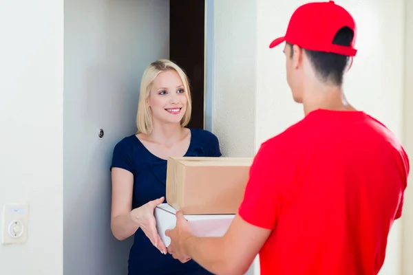 Happy young woman standing at door get her order from delivery man in red uniform