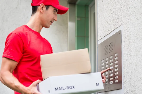 Delivery man carrying mail packages using the intercom — Stock Photo, Image