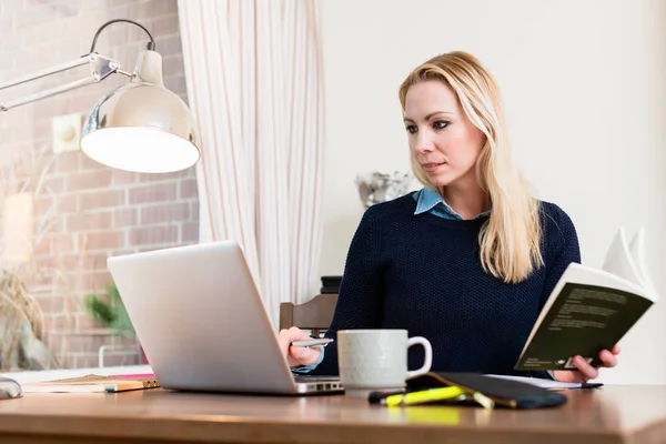 Vrouw met boek kijken naar laptop — Stockfoto