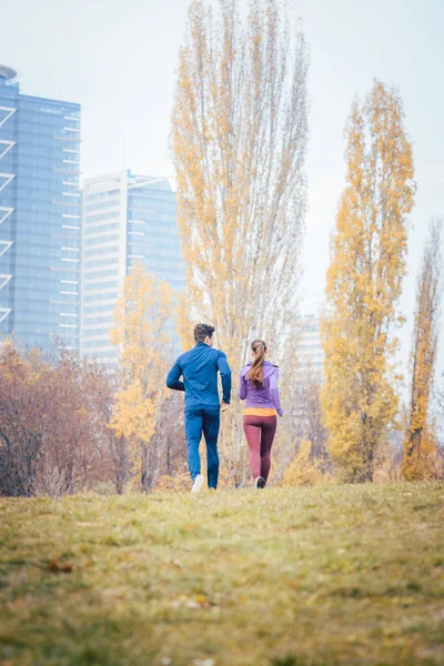 Casal visto por trás correndo através de uma cidade no outono — Fotografia de Stock