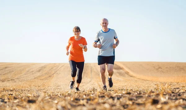 Seniorin und Mann laufen oder joggen auf Feld — Stockfoto