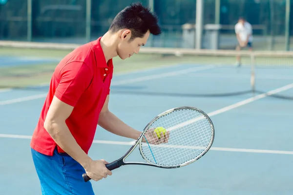 Giocatore di tennis asiatico guardando la palla con concentrazione prima di servire — Foto Stock