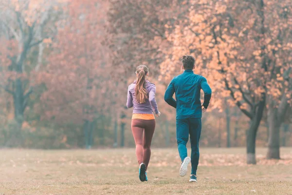 Queda correndo em um parque, visto por trás do casal — Fotografia de Stock