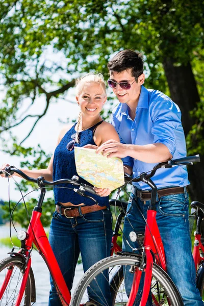 Casal segurando mapa de pé com duas bicicletas — Fotografia de Stock