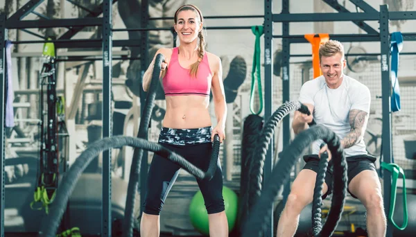 Duas mulheres bonitas e fortes acenando cordas de batalha durante o treinamento funcional — Fotografia de Stock