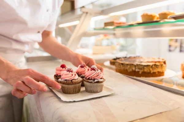 Women putting muffins on display in bakery shop — Stock Photo, Image