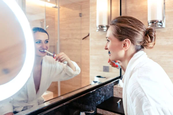 Женщина чистит зубы в роскошном отеле, глядя на себя — стоковое фото