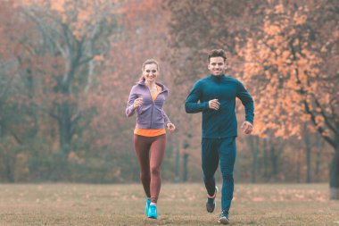 Harika sonbahar manzarası olan bir çift daha iyi spor yapmak için koşuyor.