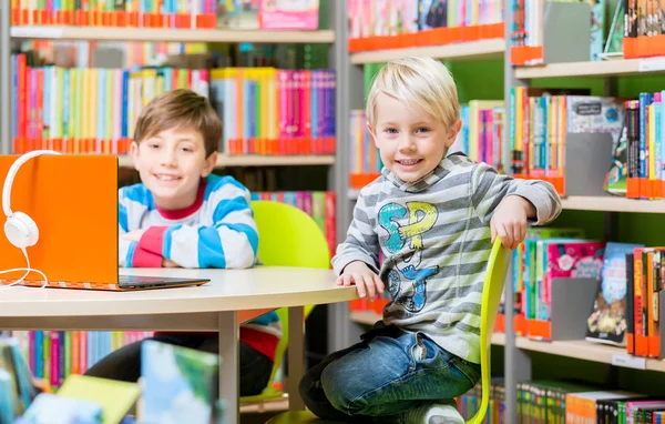 Hermanos en la biblioteca leyendo libros y escuchando audio —  Fotos de Stock