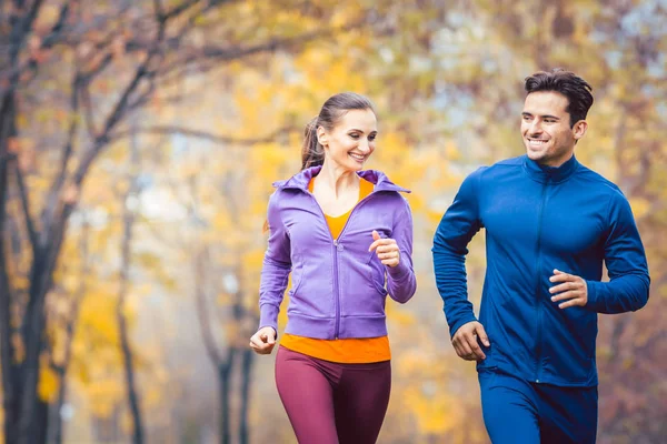 Uomo e donna che corrono come sport fitness in un parco autunnale — Foto Stock