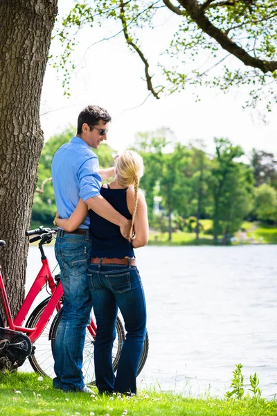 Pareja de pie cerca del lago con bicicleta — Foto de Stock