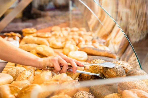 Vente femme dans boulangerie mettant pain rouleau dans un sac en papier — Photo