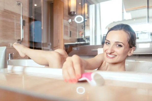 Woman having bath in hotel bathtub grabbing her shaver for hair — Stock Photo, Image