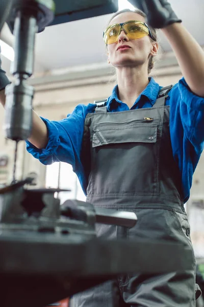 Жінка працівник в металевій майстерні використовує п'єдестал дриль — стокове фото