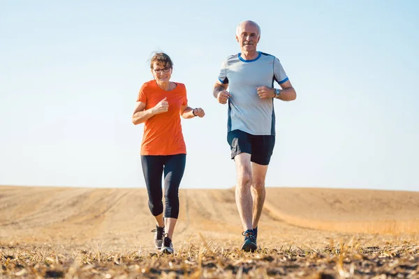 Mujer mayor y hombre corriendo o trotando en un campo — Foto de Stock