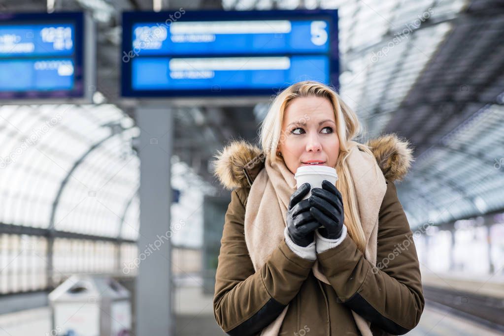 Woman in train station in cold winter warming up with a hot coffee