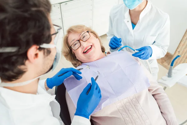 Equipe de dentistas conversando com o paciente sênior em sua cirurgia — Fotografia de Stock
